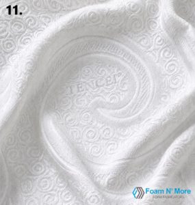 Close-up of a white Tencel mattress cover fabric featuring an embossed swirl pattern with a soft appearance that highlights the subtle stretchy texture and the quilted design.